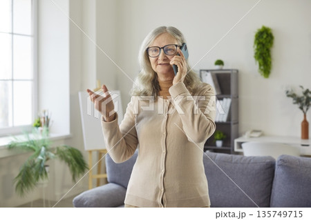 Happy senior woman talking on mobile phone with gestures and smiling at home Happy senior woman talking on mobile phone with gestures and smiling at home 135749715