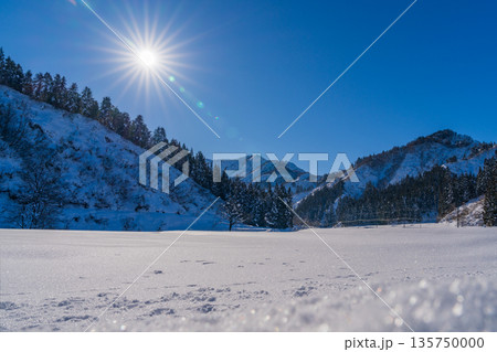冬晴れの空に輝く広大な雪原と山並み、眩しい太陽が照らす銀世界の風景 135750000