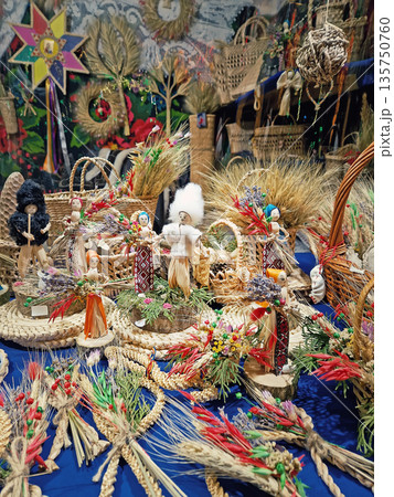 Traditional folk art features intricate wheat weavings and handmade straw dolls. Large wicker basket surrounded by colorful floral arrangements, rustic ornaments, and culturally craftsmanship 135750760