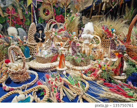 Traditional folk art features intricate wheat weavings and handmade straw dolls. Large wicker basket surrounded by colorful floral arrangements, rustic ornaments, and culturally craftsmanship Traditional folk art features intricate wheat weavings and handmade straw dolls. Large wicker basket surrounded by colorful floral arrangements, rustic ornaments, and culturally craftsmanship 135750761