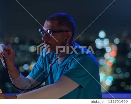 Healthcare worker wearing scrubs, focused on medical device at night 135751499