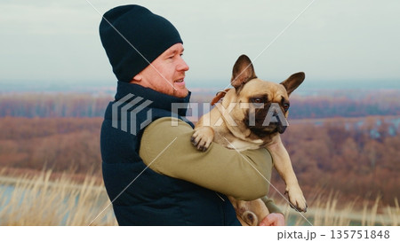 Man Holding French Bulldog in Outdoor Landscape with Scenic View of Nature in the Background During a Beautiful Daylight Setting Man Holding French Bulldog in Outdoor Landscape with Scenic View of Nature in the Background During a Beautiful Daylight Setting 135751848