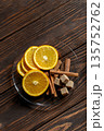 Top view of sliced oranges, cinnamon sticks and brown sugar cubes on glass plate on textured wooden surface. 135752762