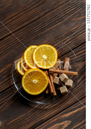 Top view of sliced oranges, cinnamon sticks and brown sugar cubes on glass plate on textured wooden surface. Top view of sliced oranges, cinnamon sticks and brown sugar cubes on glass plate on textured wooden surface. 135752762