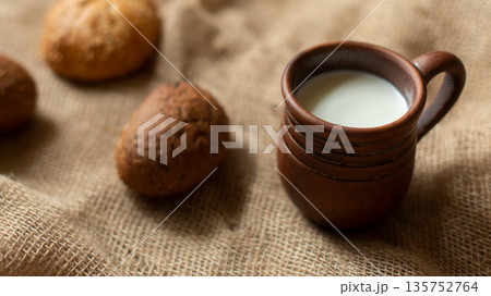 Rustic still life with fresh milk in clay mug and homemade buns on burlap background, selective focus. 135752764