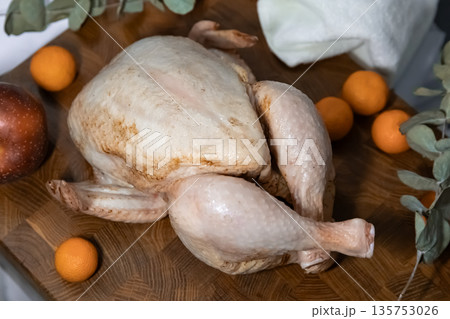 Raw whole chicken prepared for baking on a wooden cutting board with mandarins and apple. Holiday dinner preparation concept. 135753026