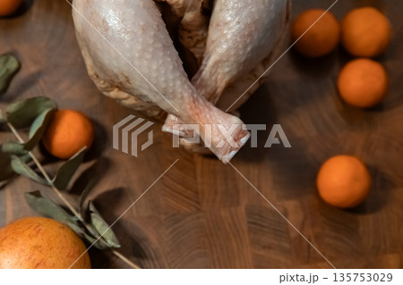 Raw whole chicken with tangerines and green branch on a wooden cutting board. Fresh poultry for cooking. Rustic kitchen background. Raw whole chicken with tangerines and green branch on a wooden cutting board. Fresh poultry for cooking. Rustic kitchen background. 135753029