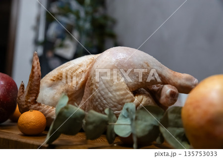 Raw turkey or chicken with apples, orange and eucalyptus leaves on a wooden table. Festive family dinner concept for Thanksgiving. Raw turkey or chicken with apples, orange and eucalyptus leaves on a wooden table. Festive family dinner concept for Thanksgiving. 135753033