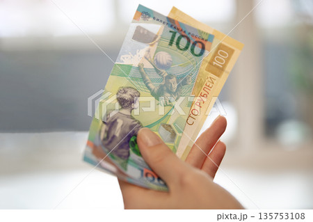 Woman hand holding two 100 ruble banknotes with football player image, representing currency, finance, and sports. Economy concept. 135753108