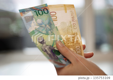 Woman holding new Russian 100 ruble banknote. Concept of economy, finance, currency exchange, payment, and budget. For investment analysis. 135753109