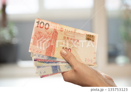 Woman holding a stack of Hong Kong dollar banknotes, including a one hundred dollar banknote. Concept of finance, wealth, business. Woman holding a stack of Hong Kong dollar banknotes, including a one hundred dollar banknote. Concept of finance, wealth, business. 135753123