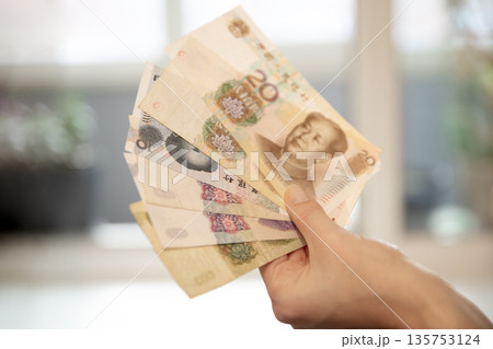 Woman hand holding Chinese yuan banknotes, showing money and financial concept. Currency exchange and personal finance theme. Woman hand holding Chinese yuan banknotes, showing money and financial concept. Currency exchange and personal finance theme. 135753124
