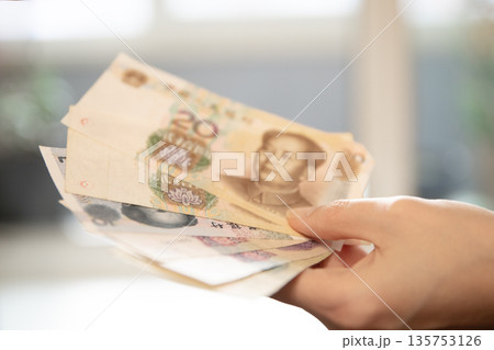Woman hand holding chinese yuan banknotes. Economic banking, finance exchange, or investment concept. Financial currency for global trade. 135753126
