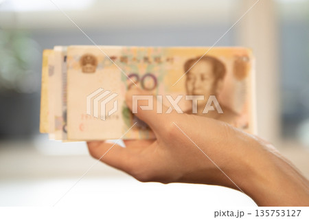 Woman hand holding Chinese Yuan banknotes. Asian currency for payment, investment, banking, and financial concept. Woman hand holding Chinese Yuan banknotes. Asian currency for payment, investment, banking, and financial concept. 135753127