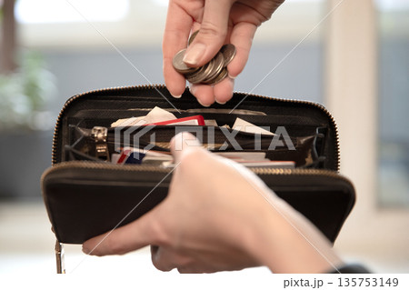 Woman putting coins into a black wallet. Financial literacy and money saving concept. Budgeting and managing personal finances. Woman putting coins into a black wallet. Financial literacy and money saving concept. Budgeting and managing personal finances. 135753149