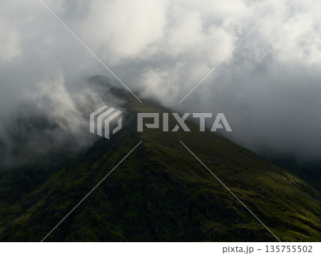 A solitary summit pierces the sky, wrapped in swirling fog and framed by green alpine growth. A solitary summit pierces the sky, wrapped in swirling fog and framed by green alpine growth. 135755502