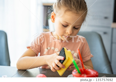 Little girl decorating Easter eggs with colorful stickers while sitting at table at home. Creative Easter activity, simple egg decoration technique and joyful holiday preparation indoors. 135757692