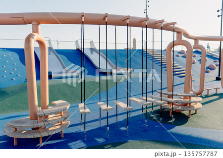 Modern playground with climbing elements and swings, showcasing safe urban design and outdoor recreation. Modern playground with climbing elements and swings, showcasing safe urban design and outdoor recreation. 135757787
