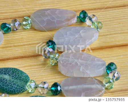 Close-up of handmade beads made of natural green and matte white agate with a crackle effect on a wooden board 135757935