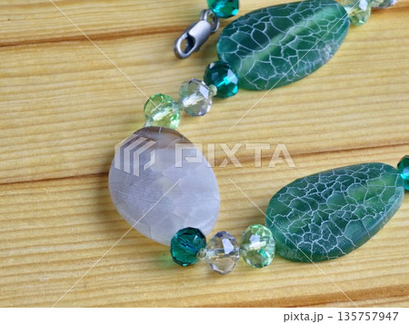 A close-up of handmade beads made of natural green and matte white agate with a crackle effect on a wooden board A close-up of handmade beads made of natural green and matte white agate with a crackle effect on a wooden board 135757947