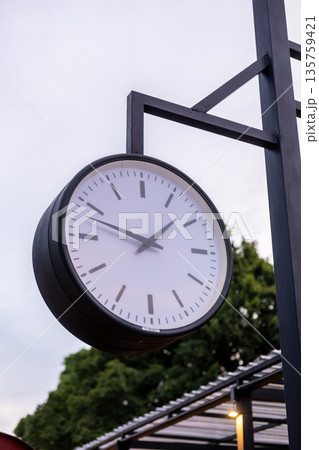 A hanging clock showing the time in outdoor space A hanging clock showing the time in outdoor space 135759421