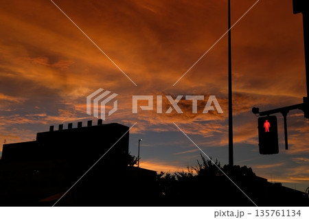 夕焼けの街に灯る赤い歩行者信号と建物のシルエット(都会の黄昏) 夕焼けの街に灯る赤い歩行者信号と建物のシルエット(都会の黄昏) 135761134