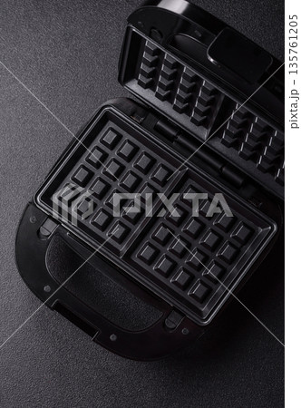A waffle iron, an electric machine for making Belgian breakfast desserts. A waffle iron A waffle iron, an electric machine for making Belgian breakfast desserts. A waffle iron 135761205