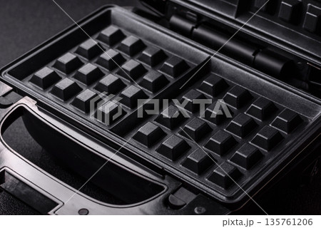 A waffle iron, an electric machine for making Belgian breakfast desserts. A waffle iron A waffle iron, an electric machine for making Belgian breakfast desserts. A waffle iron 135761206
