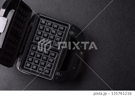A waffle iron, an electric machine for making Belgian breakfast desserts. A waffle iron A waffle iron, an electric machine for making Belgian breakfast desserts. A waffle iron 135761216