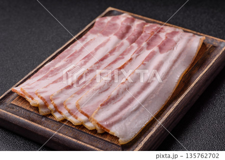 Raw smoked bacon slices, ham, jamon, or prosciutto strips for cooking. Raw bacon slices Raw smoked bacon slices, ham, jamon, or prosciutto strips for cooking. Raw bacon slices 135762702