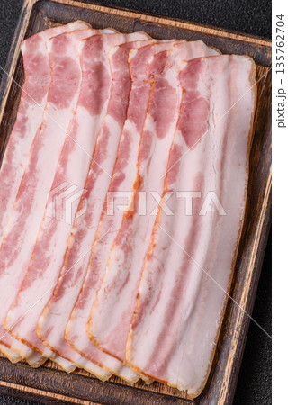Raw smoked bacon slices, ham, jamon, or prosciutto strips for cooking. Raw bacon slices Raw smoked bacon slices, ham, jamon, or prosciutto strips for cooking. Raw bacon slices 135762704