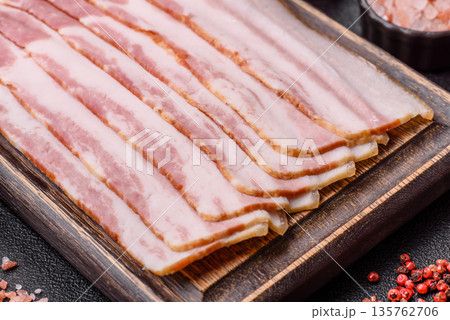 Raw smoked bacon slices, ham, jamon, or prosciutto strips for cooking. Raw bacon slices Raw smoked bacon slices, ham, jamon, or prosciutto strips for cooking. Raw bacon slices 135762706