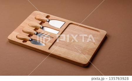 A set of cheese knives with a wooden cutting board, slicing tools. Cheese knives A set of cheese knives with a wooden cutting board, slicing tools. Cheese knives 135763928