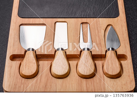 A set of cheese knives with a wooden cutting board, slicing tools. Cheese knives A set of cheese knives with a wooden cutting board, slicing tools. Cheese knives 135763936