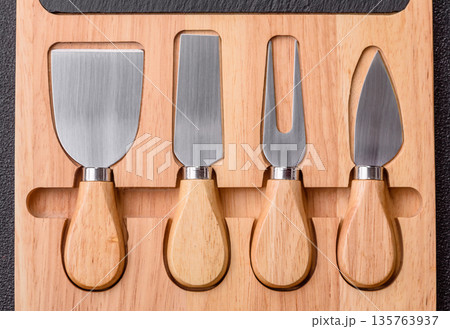 A set of cheese knives with a wooden cutting board, slicing tools. Cheese knives A set of cheese knives with a wooden cutting board, slicing tools. Cheese knives 135763937