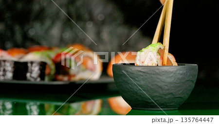 An Artistic Depiction Of Sushi Held By Bamboo Sticks Above Soy Dish Under Soft Green Illumination An Artistic Depiction Of Sushi Held By Bamboo Sticks Above Soy Dish Under Soft Green Illumination 135764447