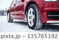 Close-Up of Winter Tires on Red Car on Snowy Road Close-Up of Winter Tires on Red Car on Snowy Road 135765192