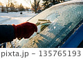 Hand in Red Glove Scraping Ice from Car Windshield on Sunny Winter Morning Hand in Red Glove Scraping Ice from Car Windshield on Sunny Winter Morning 135765193