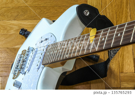 Detailed view of an electric guitar body and fretboard with a yellow pick. The instrument lies on parquet, creating a cozy atmosphere of a home studio or spring music practice Detailed view of an electric guitar body and fretboard with a yellow pick. The instrument lies on parquet, creating a cozy atmosphere of a home studio or spring music practice 135765293