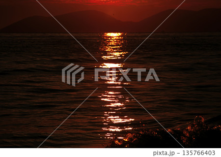 Vlora, Albania August , 2025 A serene sunset over the Adriatic Sea, with warm golden light reflecting across gentle waves and distant silhouettes of mountains. The dramatic clouds and soft evenin Vlora, Albania August , 2025 A serene sunset over the Adriatic Sea, with warm golden light reflecting across gentle waves and distant silhouettes of mountains. The dramatic clouds and soft evenin 135766403