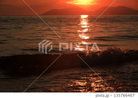 Vlora, Albania  August , 2025 A serene sunset over the Adriatic Sea, with warm golden light reflecting across gentle waves and distant silhouettes of mountains. The dramatic clouds and soft evenin 135766407