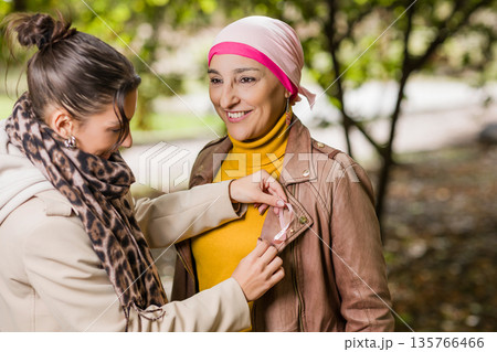 Daughter pinning breast cancer awareness ribbon on mother Daughter pinning breast cancer awareness ribbon on mother 135766466