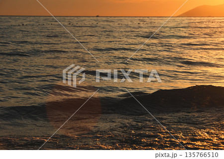 Vlora, Albania ,August , 2025 A serene sunset over the Adriatic Sea, with warm golden light reflecting across gentle waves and distant silhouettes of mountains. The dramatic clouds and soft evenin 135766510