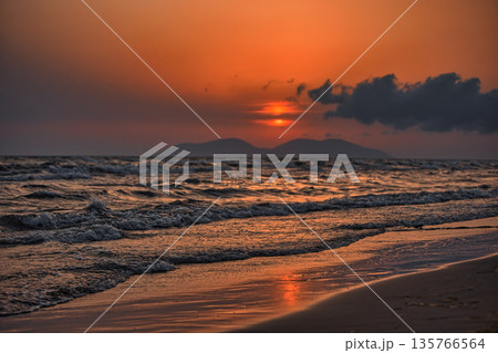 Vlora, Albania  August , 2025 A serene sunset over the Adriatic Sea, with warm golden light reflecting across gentle waves and distant silhouettes of mountains. The dramatic clouds and soft evenin 135766564