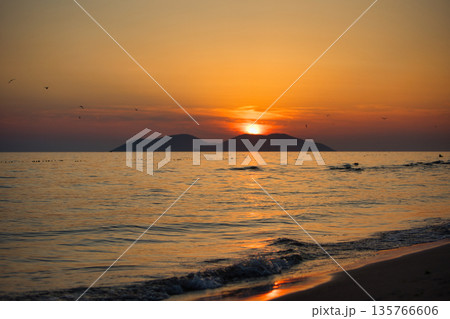 Vlora, Albania August , 2025 A serene sunset over the Adriatic Sea, with warm golden light reflecting across gentle waves and distant silhouettes of mountains. The dramatic clouds and soft evenin Vlora, Albania August , 2025 A serene sunset over the Adriatic Sea, with warm golden light reflecting across gentle waves and distant silhouettes of mountains. The dramatic clouds and soft evenin 135766606