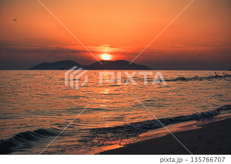 Vlora, Albania  August , 2025 A serene sunset over the Adriatic Sea, with warm golden light reflecting across gentle waves and distant silhouettes of mountains. The dramatic clouds and soft evenin 135766707