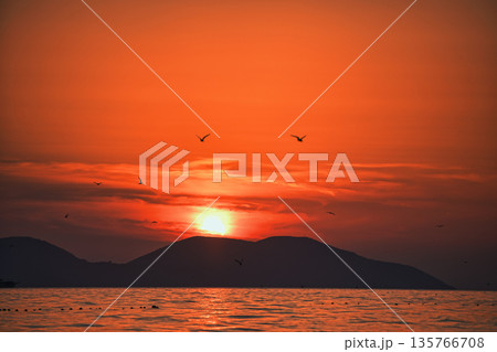 Vlora, Albania  August , 2025 A serene sunset over the Adriatic Sea, with warm golden light reflecting across gentle waves and distant silhouettes of mountains. The dramatic clouds and soft evenin 135766708