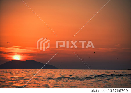 Vlora, Albania August , 2025 A serene sunset over the Adriatic Sea, with warm golden light reflecting across gentle waves and distant silhouettes of mountains. The dramatic clouds and soft evenin Vlora, Albania August , 2025 A serene sunset over the Adriatic Sea, with warm golden light reflecting across gentle waves and distant silhouettes of mountains. The dramatic clouds and soft evenin 135766709