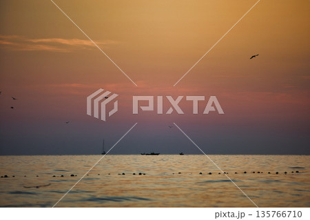 Vlora, Albania August , 2025 A serene sunset over the Adriatic Sea, with warm golden light reflecting across gentle waves and distant silhouettes of mountains. The dramatic clouds and soft evenin 135766710