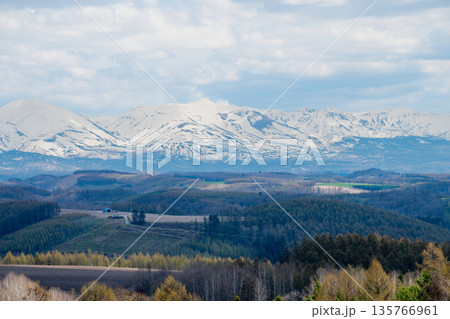 春の丘陵地帯と残雪の山頂　十勝岳 135766961